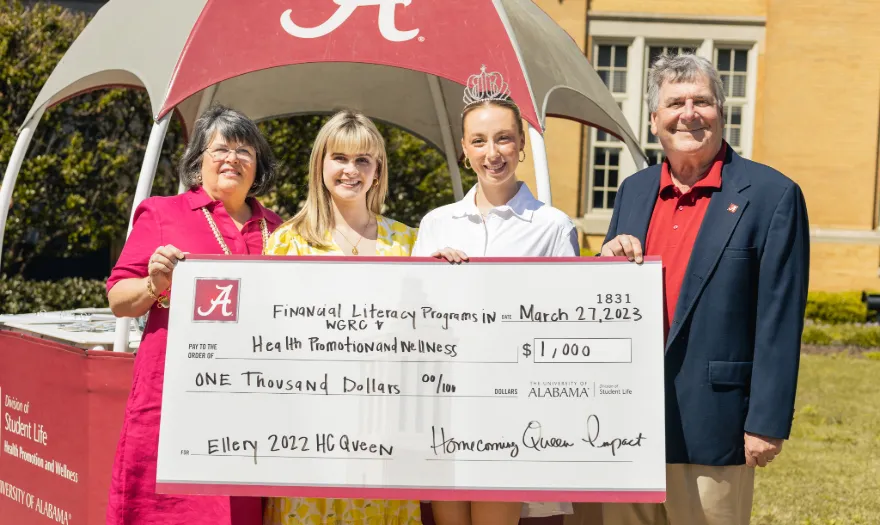 Ellery Hill and three other people holding a donation check for the UA Financial Literacy Program.